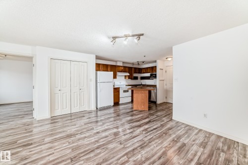 Open-concept living area featuring wood-finish flooring, a kitchen with wood cabinetry, and white appliances - 210 2305 35A Avenue, Edmonton, AB - Indoor Photo Showing Kitchen