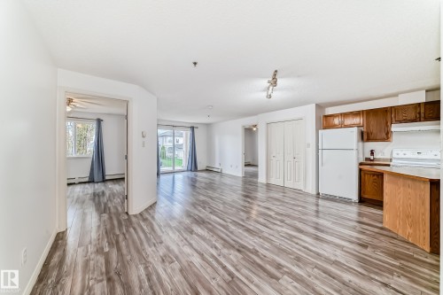 Open-concept living area featuring wood-finish flooring, white walls, and a sliding glass door leading to outdoor space - 210 2305 35A Avenue, Edmonton, AB - Indoor Photo Showing Kitchen