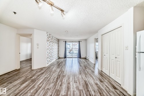 Spacious living area featuring wood-finish flooring, a decorative accent wall, and track lighting - 210 2305 35A Avenue, Edmonton, AB - Indoor Photo Showing Other Room