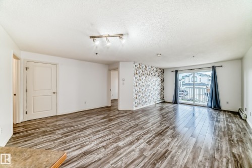 Spacious room featuring wood-finish flooring, a decorative accent wall, and track lighting - 210 2305 35A Avenue, Edmonton, AB - Indoor Photo Showing Other Room