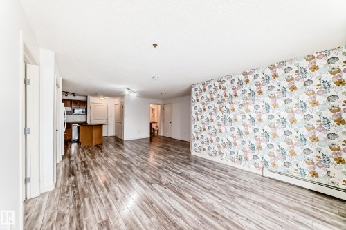 Spacious interior featuring wood-finish flooring, a decorative accent wall with a floral pattern, and track lighting - 210 2305 35A Avenue, Edmonton, AB - Indoor