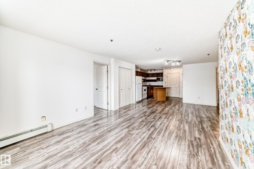 Open-concept living area with wood-finish flooring, a feature wall with floral wallpaper, and neutral white walls - 210 2305 35A Avenue, Edmonton, AB - Indoor