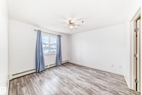 Spacious room featuring wood-finish flooring, a window with exterior views, and a ceiling fan light fixture - 210 2305 35A Avenue, Edmonton, AB - Indoor Photo Showing Other Room