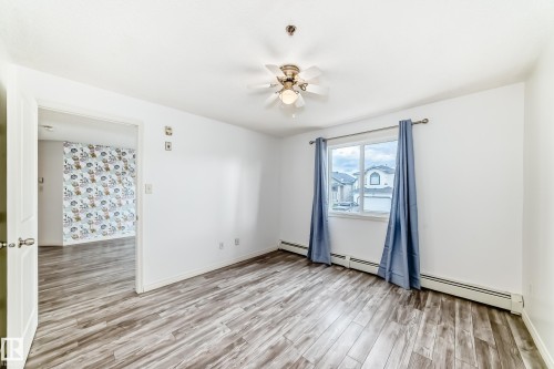 Spacious room featuring wood-finish flooring, a ceiling fan with integrated lighting, a large window, and baseboard heating - 210 2305 35A Avenue, Edmonton, AB - Indoor Photo Showing Other Room