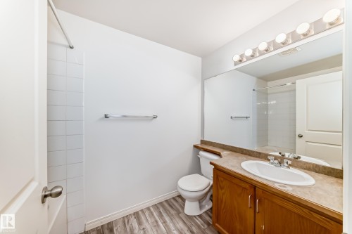Bathroom featuring a single vanity with wood-finish cabinetry, a large mirror, and a five-light fixture - 210 2305 35A Avenue, Edmonton, AB - Indoor Photo Showing Bathroom