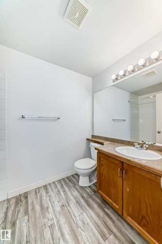 Bathroom featuring wood-finish flooring, a wood-finish vanity with an integrated sink, a large mirror, a six-bulb vanity light fixture, and a built-in shower enclosure - 210 2305 35A Avenue, Edmonton, AB - Indoor Photo Showing Bathroom