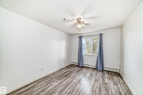 Interior room featuring wood-finish flooring, a ceiling fan with integrated lighting, and a window with a curtain rod - 210 2305 35A Avenue, Edmonton, AB - Indoor Photo Showing Other Room