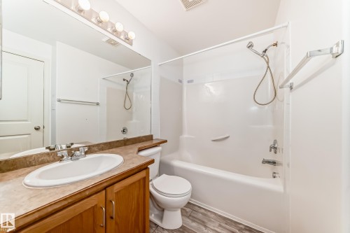 Bathroom featuring a wood-finish vanity with an integrated sink, a large wall-mounted mirror, a tub/shower combination, and wood-finish flooring - 210 2305 35A Avenue, Edmonton, AB - Indoor Photo Showing Bathroom
