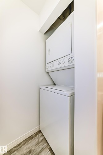 Dedicated laundry area featuring a stacked white washer and dryer unit, white walls, and wood-finish flooring - 210 2305 35A Avenue, Edmonton, AB - Indoor Photo Showing Laundry Room