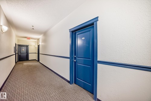 Hallway featuring a textured off-white wall finish, blue accent trim, and a patterned carpet runner - 210 2305 35A Avenue, Edmonton, AB - Indoor Photo Showing Other Room