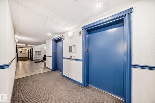 Corridor featuring two elevators with blue doors and trim, recessed lighting, and wall-mounted sconces - 210 2305 35A Avenue, Edmonton, AB - Indoor Photo Showing Other Room