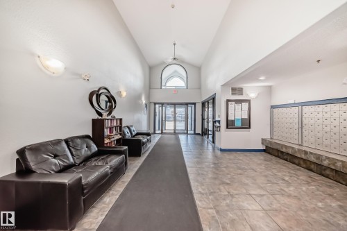 Main entrance foyer featuring vaulted ceilings, a prominent arched window, tiled flooring, built-in mailboxes, and wall sconce lighting - 210 2305 35A Avenue, Edmonton, AB - Indoor Photo Showing Other Room