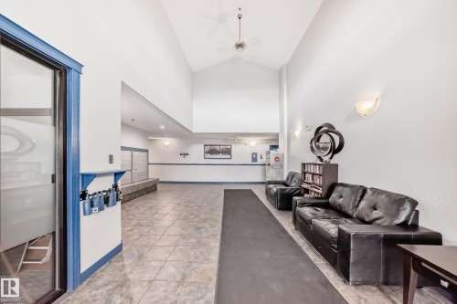 Spacious entry foyer featuring vaulted ceilings, tile flooring, wall-mounted sconce lighting, and a mail area with built-in bench seating - 210 2305 35A Avenue, Edmonton, AB - Indoor Photo Showing Other Room