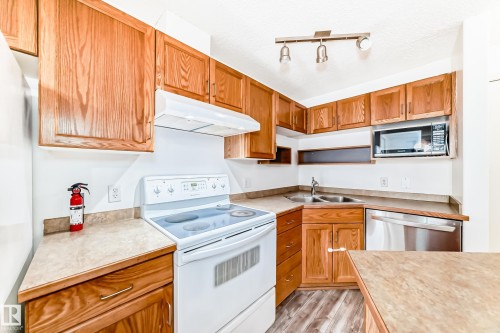 Kitchen featuring wood-finish cabinetry, white appliances, and laminate countertops - 210 2305 35A Avenue, Edmonton, AB - Indoor Photo Showing Kitchen With Double Sink