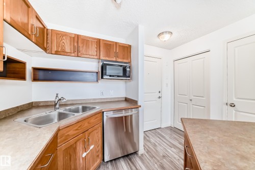 Kitchen area featuring wood cabinetry, a double basin stainless steel sink, and stainless steel dishwasher - 210 2305 35A Avenue, Edmonton, AB - Indoor Photo Showing Kitchen With Double Sink