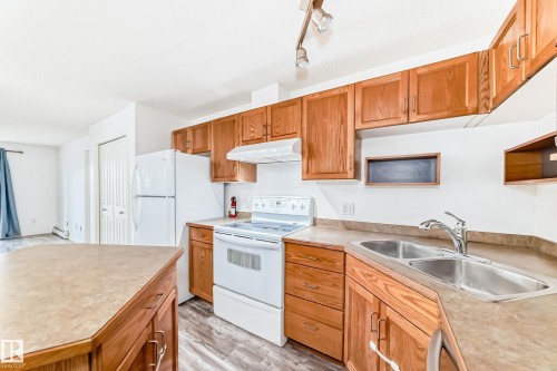 Kitchen featuring wood cabinetry, laminate countertops, a double basin stainless steel sink, and white appliances including a range and refrigerator - 210 2305 35A Avenue, Edmonton, AB - Indoor Photo Showing Kitchen With Double Sink
