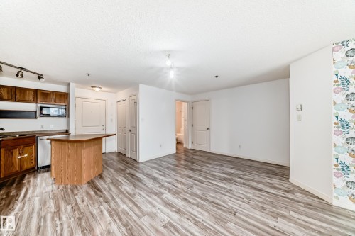 Open-concept living area featuring wood-finish flooring, a kitchen island with seating, dark wood cabinetry, and a built-in microwave - 210 2305 35A Avenue, Edmonton, AB - Indoor Photo Showing Kitchen