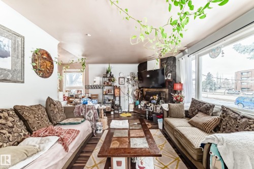 Living area featuring large windows, a stone fireplace, and hard flooring - 7723 82 Avenue, Edmonton, AB - Indoor Photo Showing Living Room