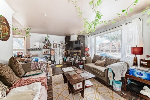 The living area features a large picture window, a stone-clad fireplace, and dark hardwood flooring - 7723 82 Avenue, Edmonton, AB - Indoor Photo Showing Living Room