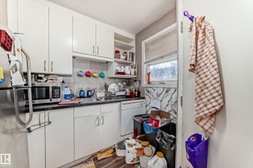 The kitchen features white cabinetry, a stainless steel refrigerator, and a window with blinds - 7723 82 Avenue, Edmonton, AB - Indoor