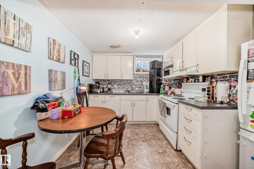 The kitchen area features light-colored cabinetry, a dark countertop, and a grey brick-patterned backsplash - 7723 82 Avenue, Edmonton, AB - Indoor Photo Showing Kitchen With Double Sink