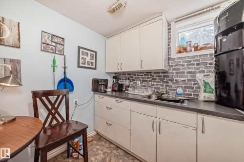 The property includes a kitchen area with white cabinetry, a dark countertop, a single basin sink, and a window above the sink - 7723 82 Avenue, Edmonton, AB - Indoor Photo Showing Kitchen With Double Sink