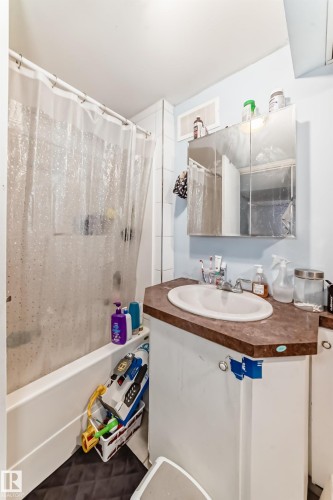 Bathroom featuring a bathtub with a shower, a vanity with a countertop and an integrated sink, and a mirrored medicine cabinet - 7723 82 Avenue, Edmonton, AB - Indoor Photo Showing Bathroom