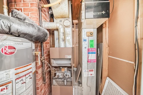 The property is equipped with a Rheem water heater, a furnace unit, and an air handling unit, all visible against a brick wall and wood framing - 7723 82 Avenue, Edmonton, AB - Indoor Photo Showing Basement