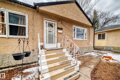 The property features a stucco exterior, a front entry with a white storm door, and a staircase leading to the entrance - 7723 82 Avenue, Edmonton, AB - Outdoor
