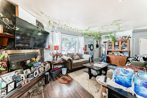 This living area features hardwood flooring and a stone-clad fireplace - 7723 82 Avenue, Edmonton, AB - Indoor Photo Showing Living Room