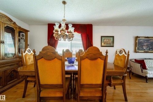 Formal dining area featuring wood-finish flooring, a decorative chandelier, and window with red drapery - 8509 39B Avenue, Edmonton, AB - Indoor Photo Showing Dining Room