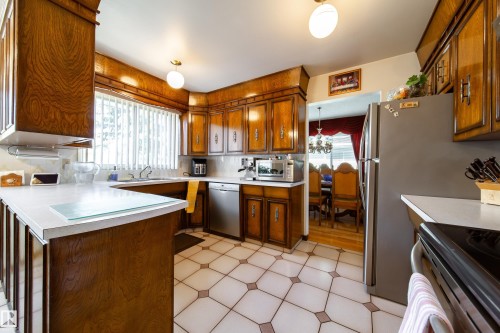 Kitchen featuring wood cabinetry, white countertops, stainless steel dishwasher, and patterned tile flooring - 8509 39B Avenue, Edmonton, AB - Indoor Photo Showing Kitchen