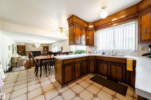 Open-concept kitchen featuring wood-finish cabinetry, a corner sink with a large window, light-toned countertops, and geometric tile flooring - 8509 39B Avenue, Edmonton, AB - Indoor Photo Showing Kitchen