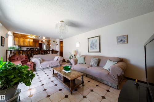 Living area featuring octagonal tile flooring with contrasting diamond inserts, a crystal chandelier, and a wood railing overlooking a kitchen with wood cabinetry - 8509 39B Avenue, Edmonton, AB - Indoor Photo Showing Living Room