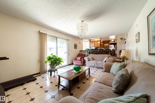Expansive living area featuring tile flooring with decorative inserts, a sliding glass door, and an overhead chandelier - 8509 39B Avenue, Edmonton, AB - Indoor Photo Showing Living Room