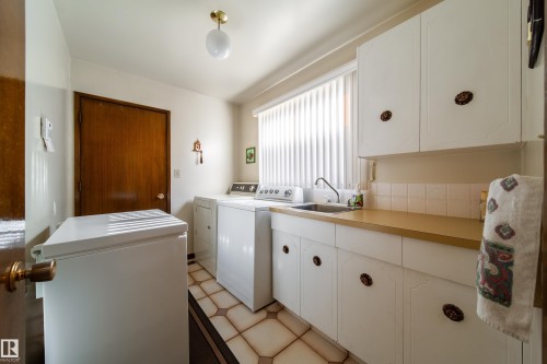 Functional utility room featuring white cabinetry, a single-basin sink, and a window with vertical blinds - 8509 39B Avenue, Edmonton, AB - Indoor Photo Showing Laundry Room