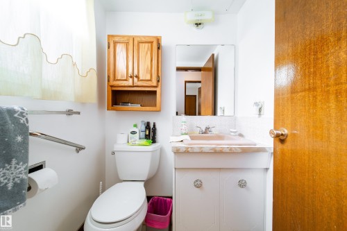 Bathroom featuring a light-colored vanity with a built-in sink, a wall-mounted mirror, and a wood-finish cabinet - 8509 39B Avenue, Edmonton, AB - Indoor Photo Showing Bathroom