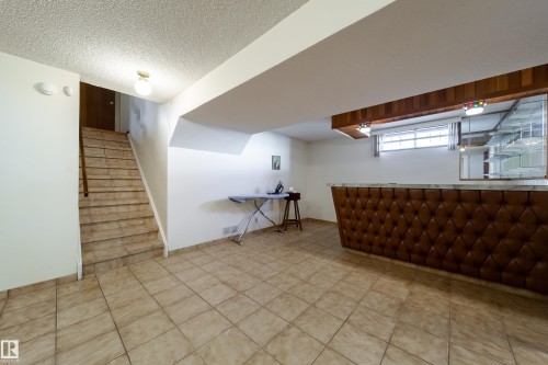 Finished lower level featuring a built-in bar with tufted brown paneling and a light-toned countertop, complemented by overhead wood-finish cabinetry - 8509 39B Avenue, Edmonton, AB - Indoor