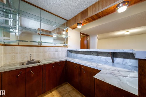 Wet bar featuring a stainless steel sink, patterned tile backsplash, and extensive glass shelving - 8509 39B Avenue, Edmonton, AB - Indoor Photo Showing Kitchen