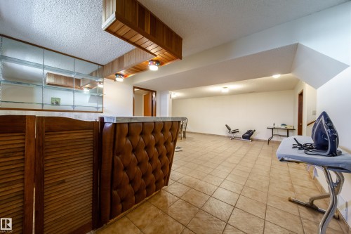 Recreation room featuring a built-in bar with wood paneling and tufted upholstery, a marble-finish countertop, and integrated ceiling lighting - 8509 39B Avenue, Edmonton, AB - Indoor