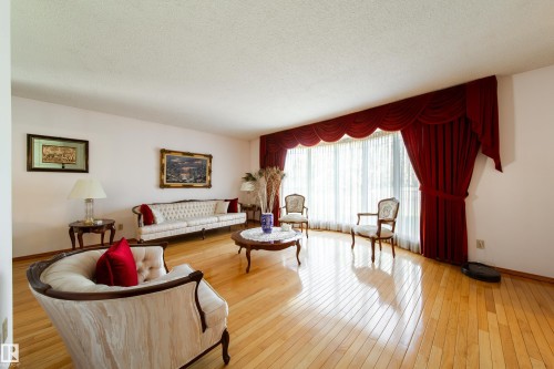 Expansive room featuring light wood-finish flooring, a large bay window with full-length drapery, and a textured white ceiling - 8509 39B Avenue, Edmonton, AB - Indoor Photo Showing Living Room