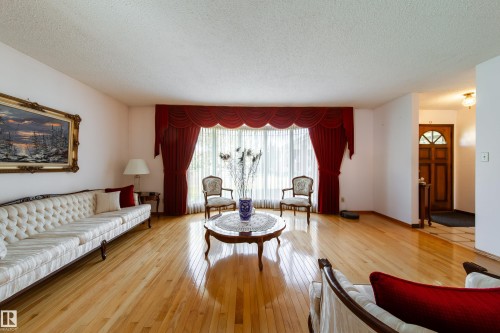 Spacious living area featuring polished wood-finish flooring, a large picture window with valance and drapes, and an adjacent entry foyer with a decorative wood door - 8509 39B Avenue, Edmonton, AB - Indoor Photo Showing Living Room