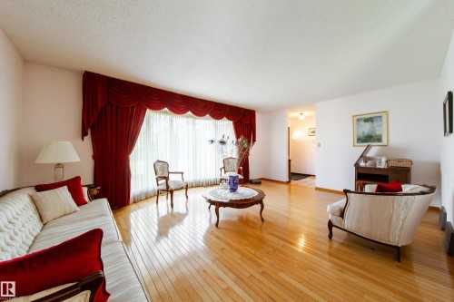 Living area featuring lustrous wood-finish flooring, a large bay window with decorative valances, and light-toned walls - 8509 39B Avenue, Edmonton, AB - Indoor Photo Showing Living Room