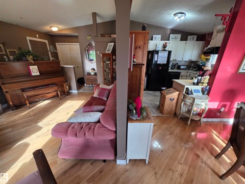 Open-concept living area featuring wood-finish flooring, vaulted ceiling, and a kitchen with white cabinetry and black appliances - 25 Mcnabb Crescent, Stony Plain, AB - Indoor