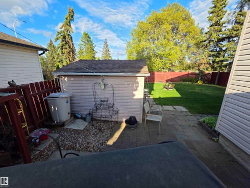 Spacious backyard featuring a manicured lawn, red picket fencing, and mature trees - 25 Mcnabb Crescent, Stony Plain, AB - Outdoor With Deck Patio Veranda