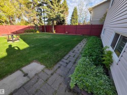 Fenced backyard featuring a manicured lawn, established perimeter landscaping, and a paver pathway - 