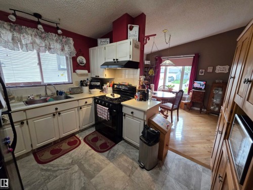 Kitchen with white cabinetry, a black oven range, and a stainless steel sink, featuring a light-colored countertop - 25 Mcnabb Crescent, Stony Plain, AB - Indoor Photo Showing Kitchen With Double Sink