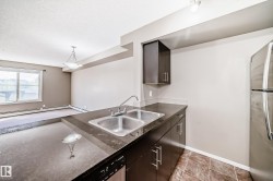 Kitchen featuring a double basin stainless steel sink, dark cabinetry, and coordinating dark countertops - 