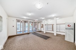 Building entry featuring a glass door system, wall-mounted mailboxes, parcel locker access, and recessed ceiling lighting - 