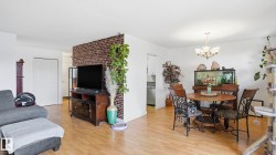 Open-concept living space featuring wood-finish flooring, a dining area with a chandelier, and a partial brick-accent wall - 